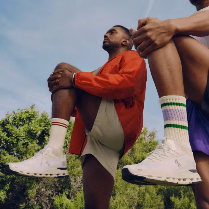 A pair of athletes stretch, wearing On running shoes.