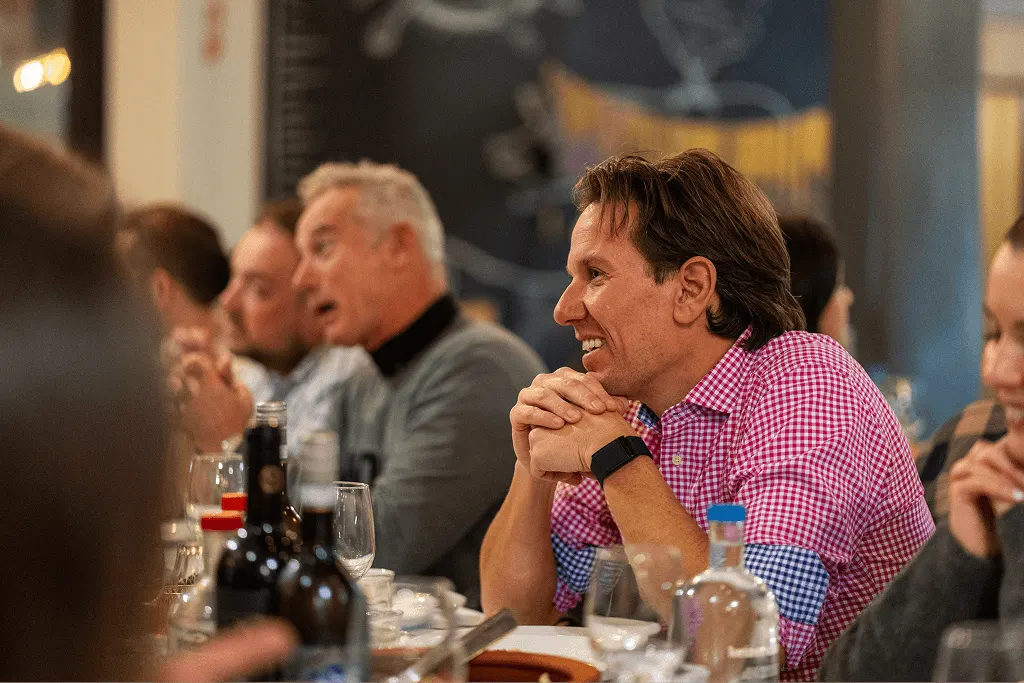 Smiling person in red checkered shirt sits at restaurant bar with others, enjoying conversation in warm evening ambiance
