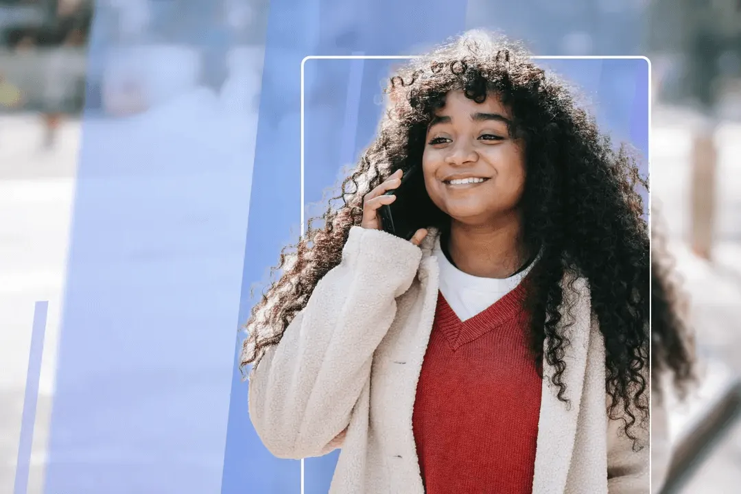 Young woman with long curly hair smiling warmly, wearing a red sweater and beige cardigan talking on mobile phone.