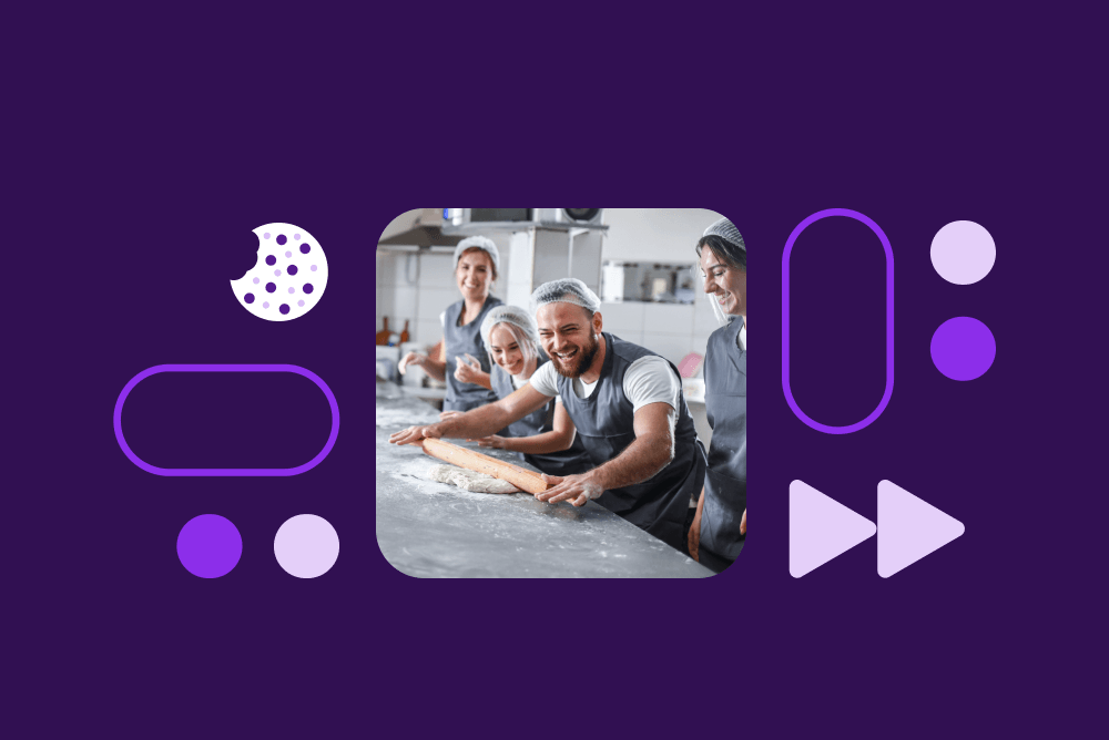 Bakers working together in a commercial kitchen, rolling dough on a flour-dusted counter, surrounded by purple decorative elements