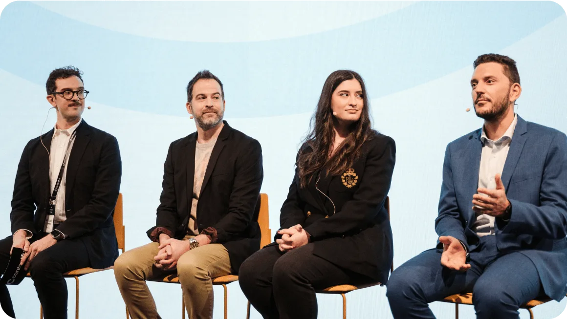 Four business professionals seated on orange chairs during a panel discussion against a light blue background