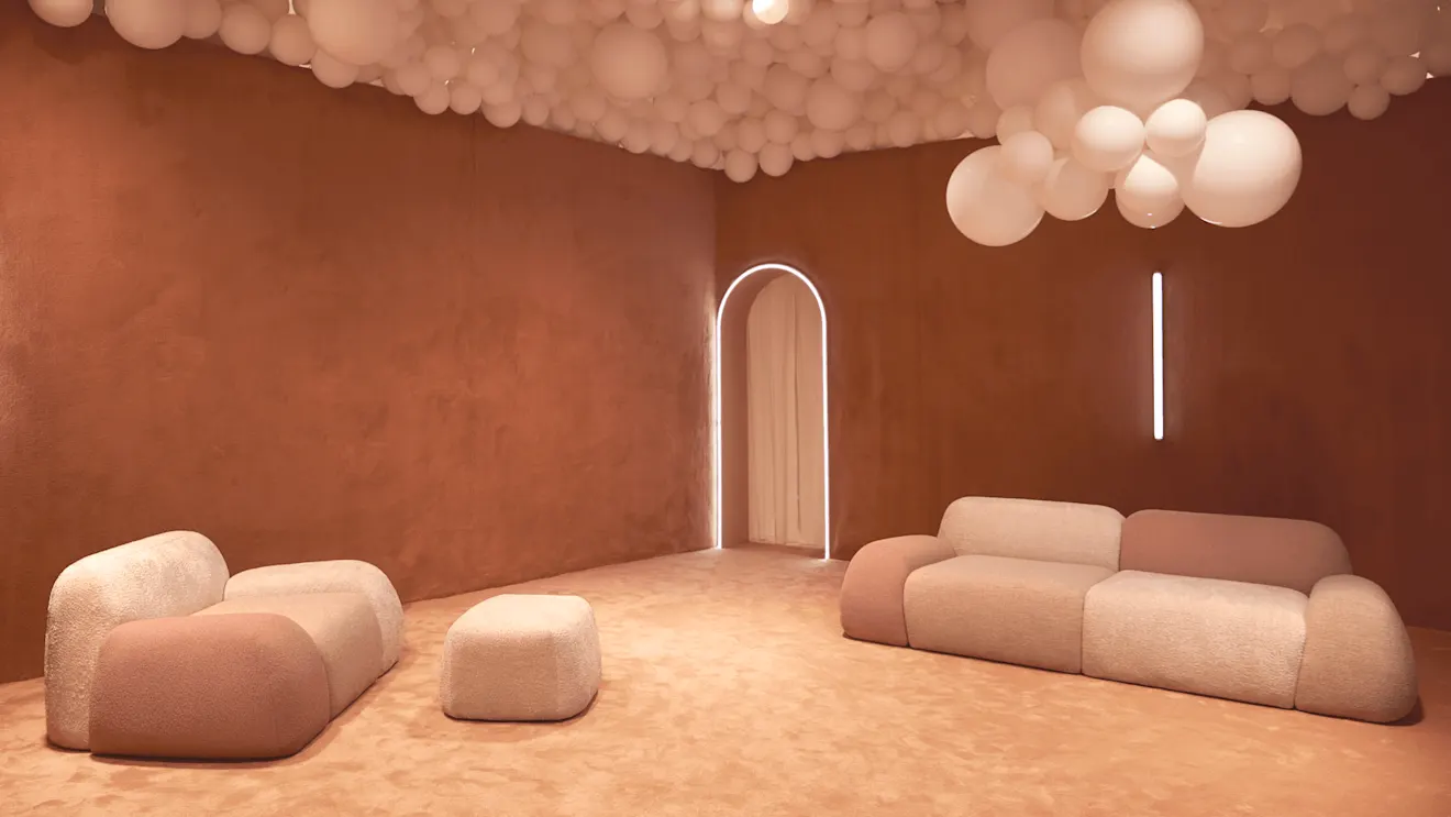 A warm terracotta room with cream bouclé sofas, white balloon ceiling installation, and a glowing arched doorway.