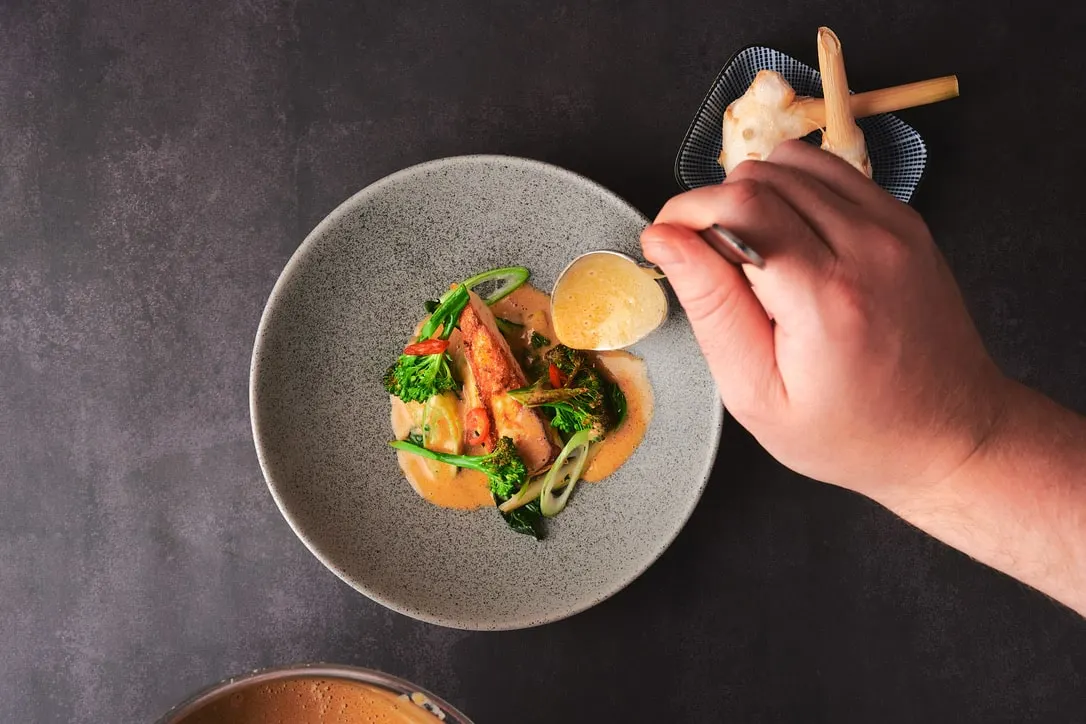 Plated Asian dish with broccoli and chicken in orange sauce, served on a textured grey plate with decorative garnish