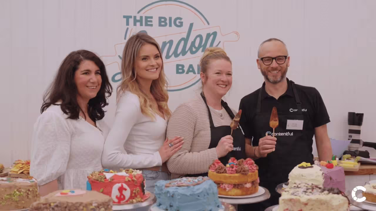 Group of smiling people standing behind a table displaying colorful decorated cakes at "The Big London Bake" event