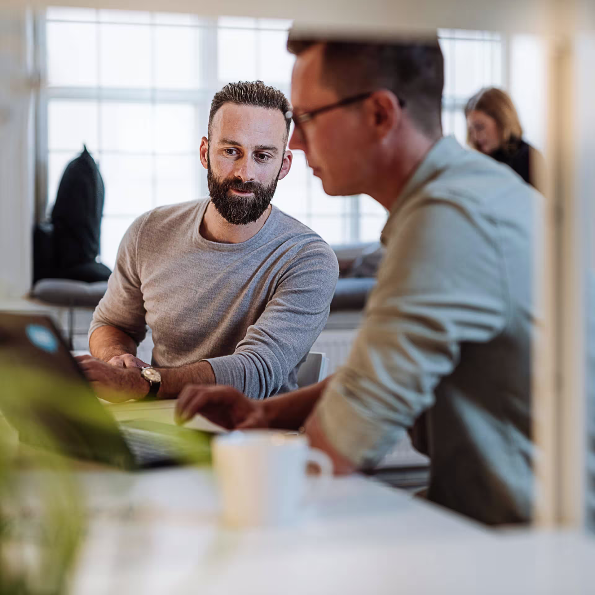 Two professionals in casual office attire having a focused discussion while reviewing documents at a bright, modern workspace