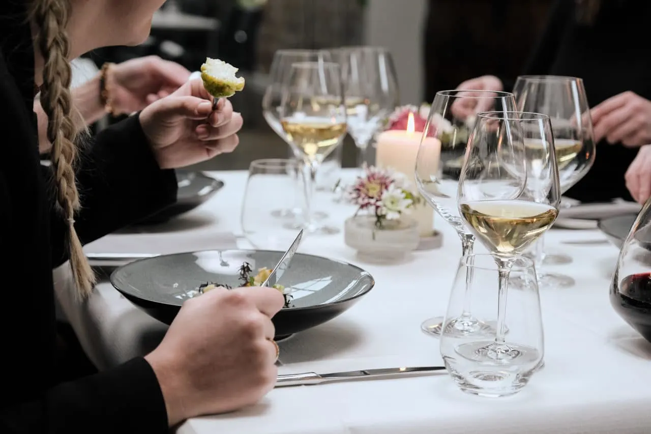 Elegant dinner table setting with white wine glasses, lit candles, and floral decorations as diners enjoy their meal in dim lighting