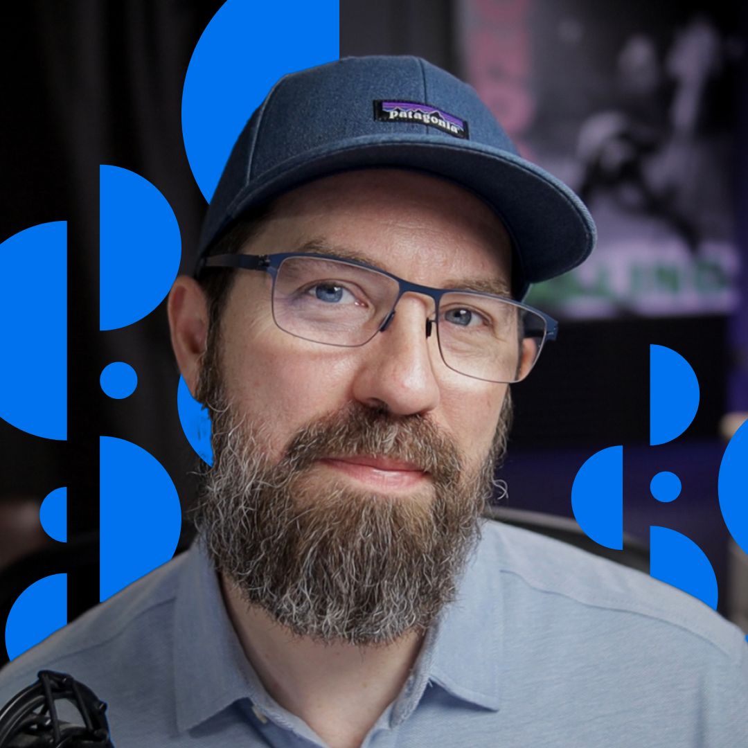A middle-aged man with a hat and glasses in his studio, and some artwork composited in.