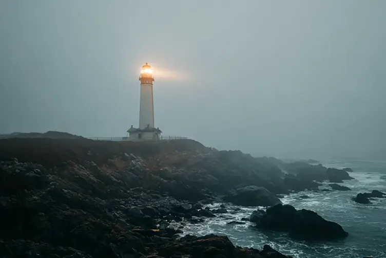A lighthouse's light piercing through the fog on the coast