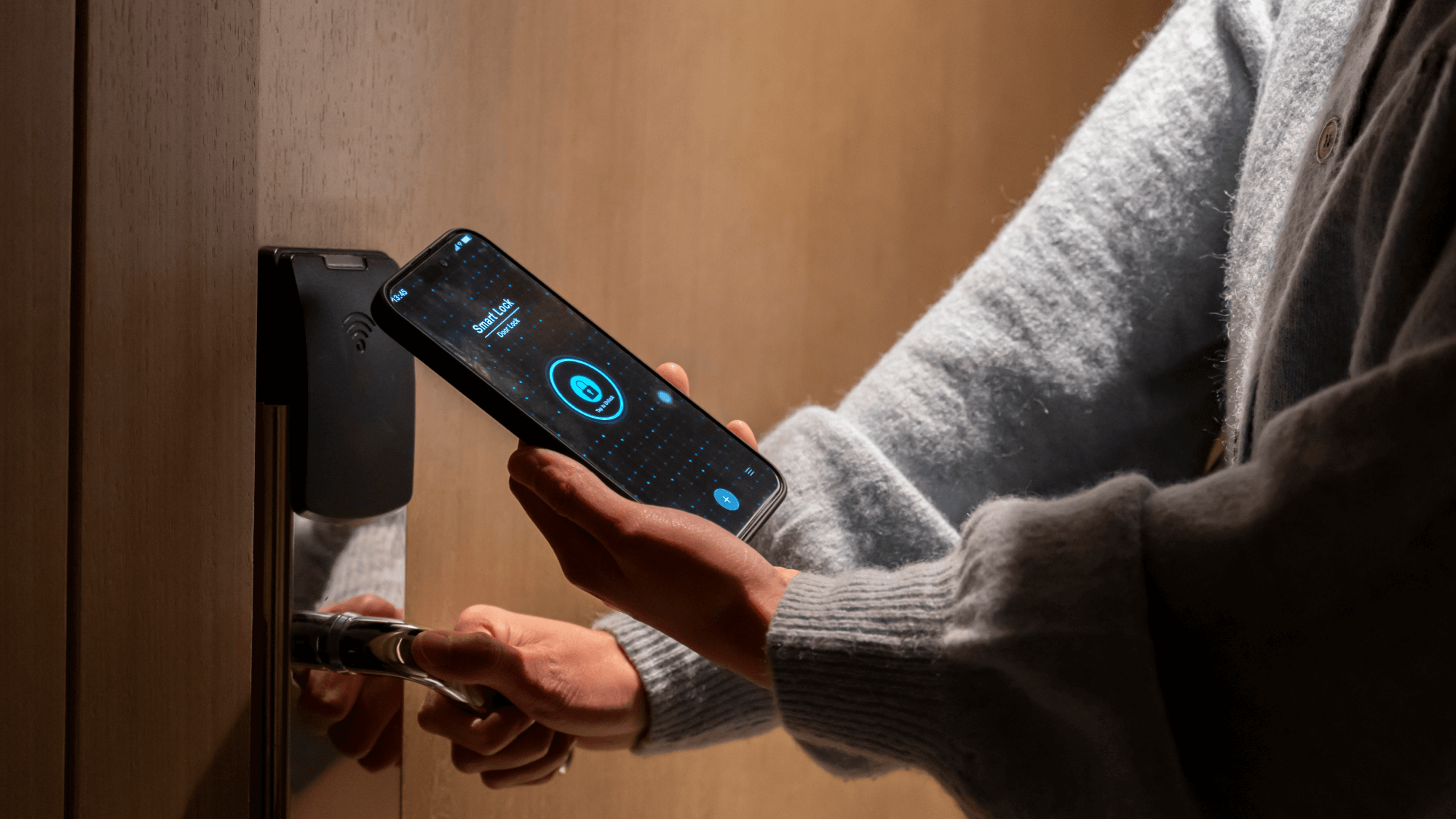 Person in gray sweater using smartphone to unlock door with digital smart lock system showing blue interface screen