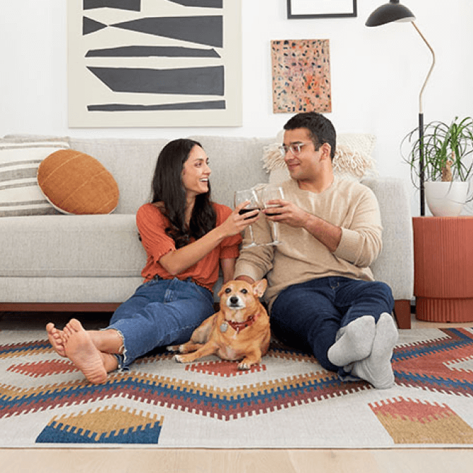 Couple relaxing on a geometric art rug with wine glasses and their golden dog