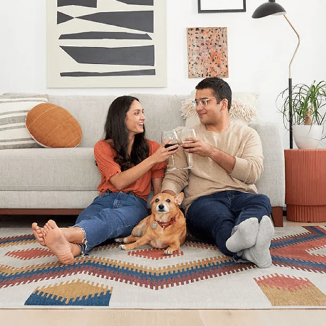 Couple relaxing on a geometric art rug with wine glasses and their golden dog