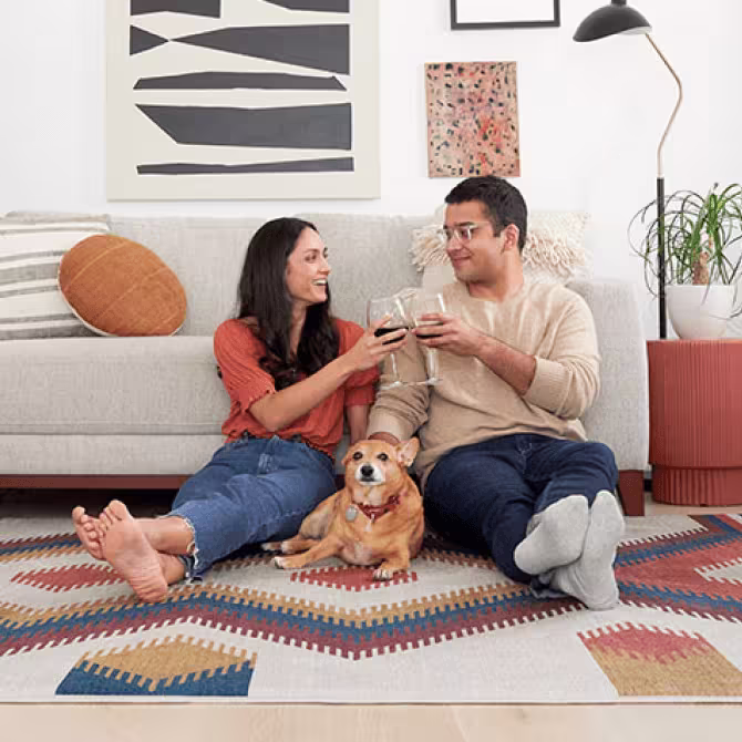 Couple relaxing on a geometric art rug with wine glasses and their golden dog