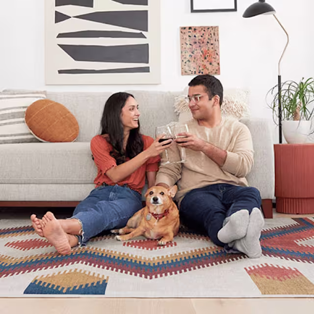 Couple relaxing on a geometric art rug with wine glasses and their golden dog