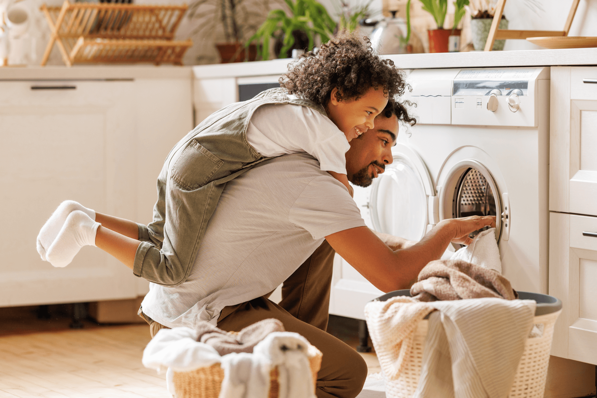 Parent and child doing laundry together in bright modern laundry room, loading clothes into washing machine