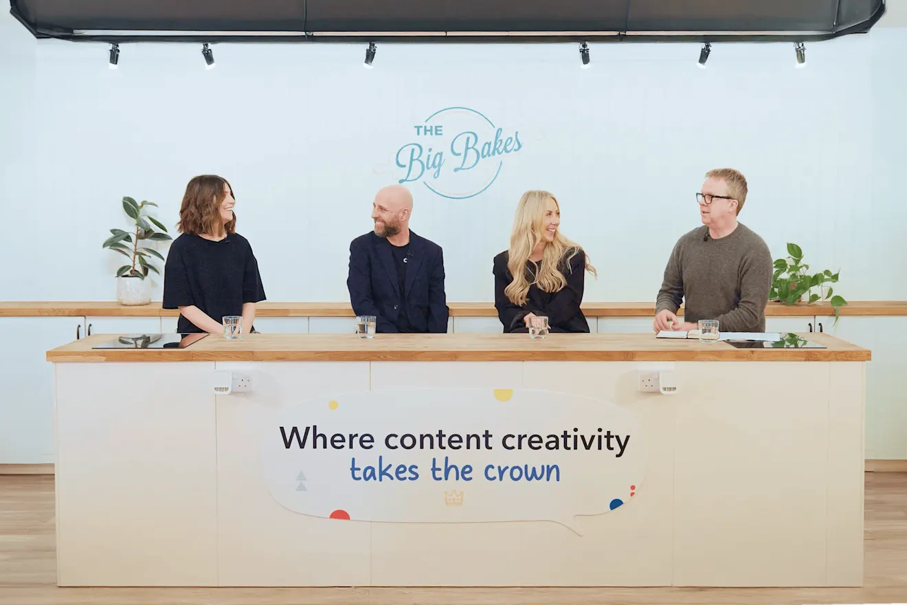 Four team members seated at a desk with "The Big Bakes" logo and text "Where content creativity takes the crown" on wall behind them