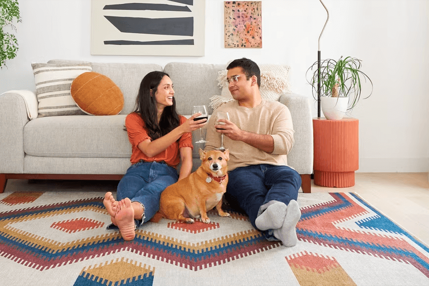 Couple relaxing on a geometric art rug with wine glasses and their cute golden dog