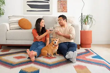 Couple relaxing on a geometric art rug with wine glasses and their cute golden dog