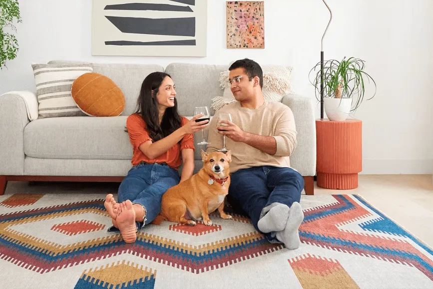 Couple relaxing on a geometric art rug with wine glasses and their cute golden dog