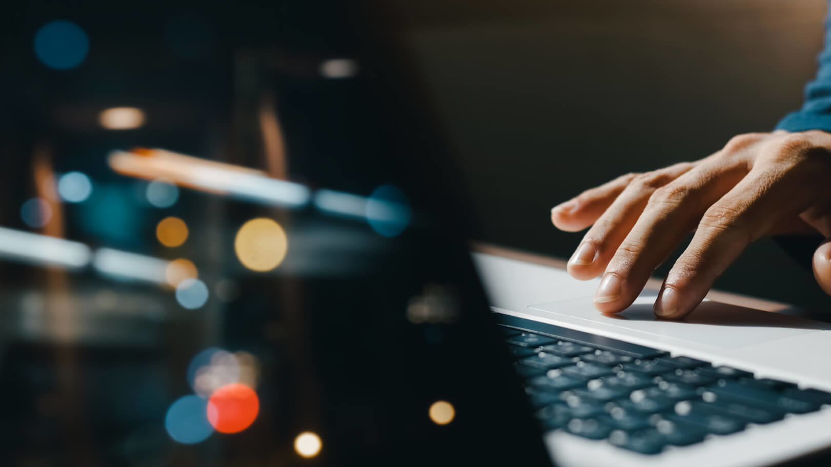 Hand using laptop touchpad against dark background with blurred colorful bokeh lights