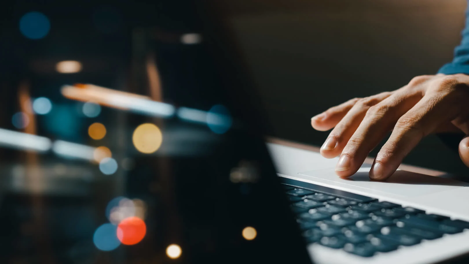Hand using laptop touchpad against dark background with blurred colorful bokeh lights