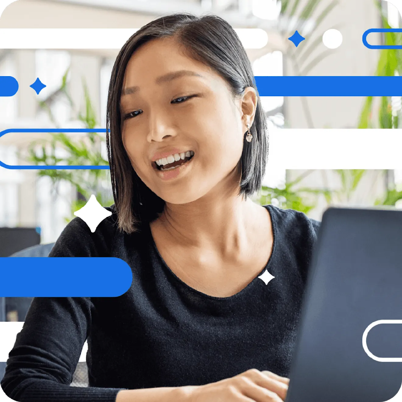 Professional in black sweater smiling warmly while working on laptop in bright office with plants and blue geometric decorations