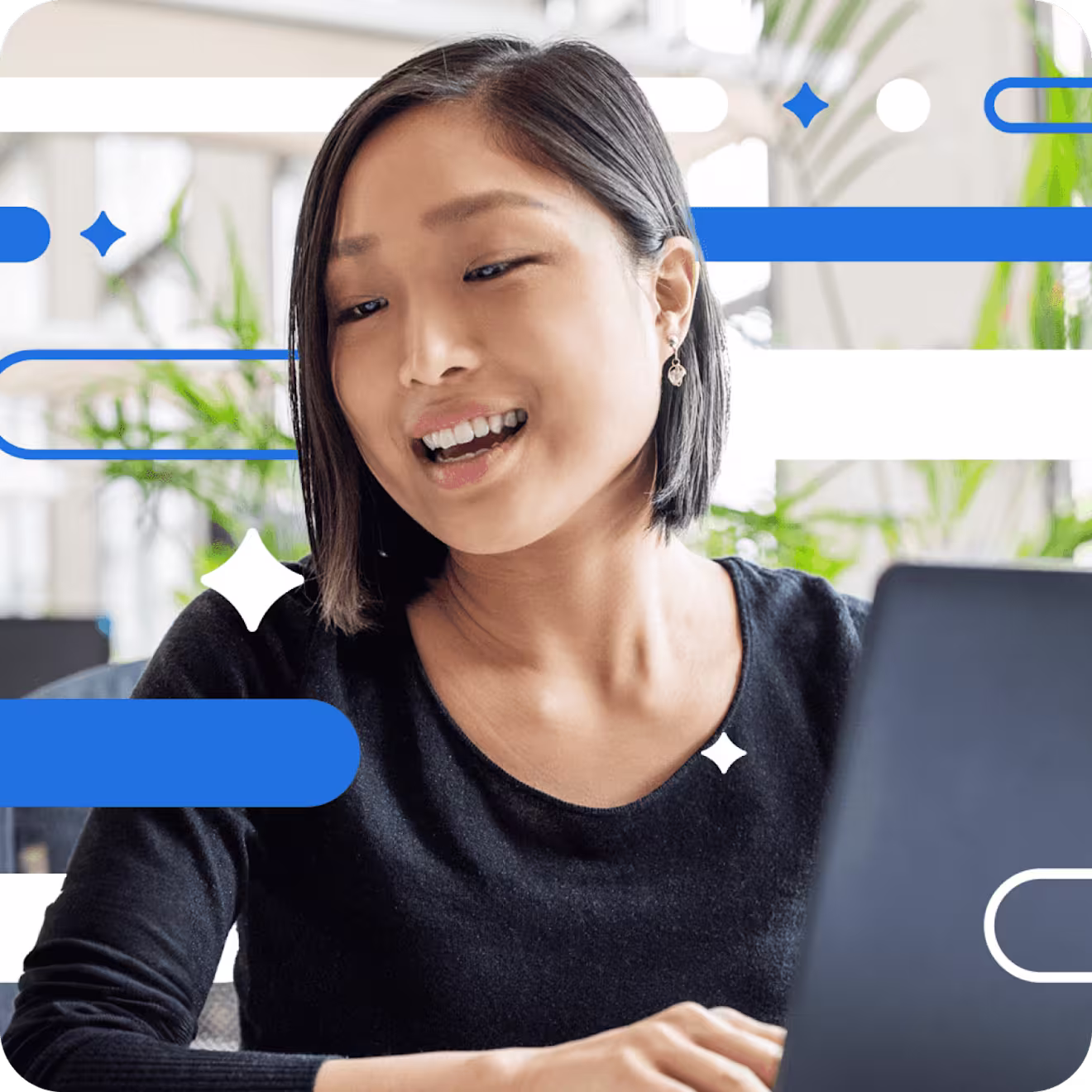 Professional in black sweater smiling warmly while working on laptop in bright office with plants and blue geometric decorations