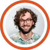 Smiling person with curly brown hair and glasses wearing a light blue shirt against an orange circular background