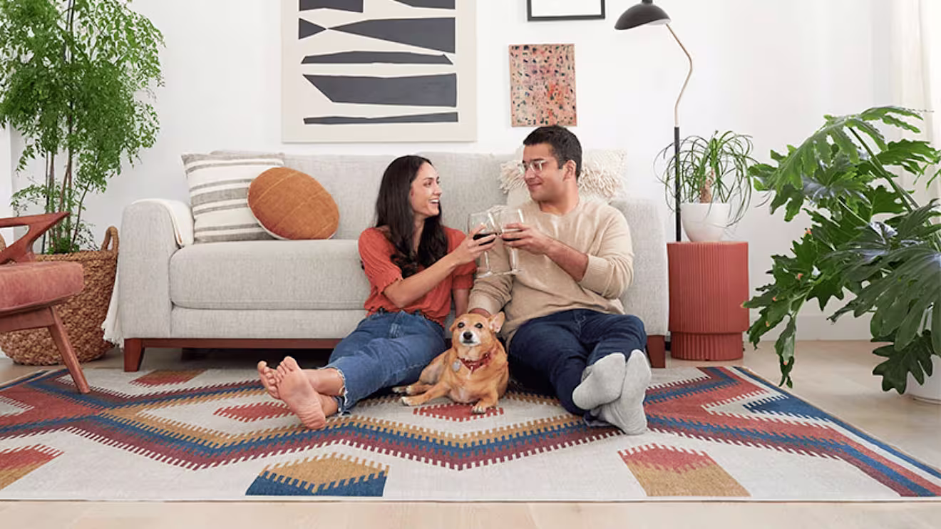 Couple relaxing on a geometric art rug with wine glasses and their golden dog